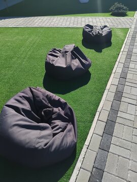 Row of grey bean bag chairs on green artificial lawn outdoors