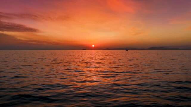 Slow motion view of a calm ocean during a beautiful sunset with orange and red clouds and reflections in the water