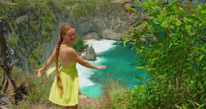 Happy female traveler in summer dress looking at beautiful coastal landscape with turquoise ocean bay in Nusa Penida Bali Island Indonesia