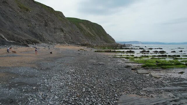 Aerial view of rocky coastline and beach with mossy rock formations and people walking along the shore in Bilbao, Basque Country, Spain.