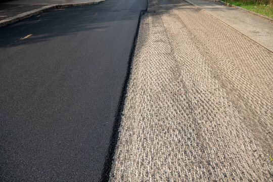 Milled asphalt road surface texture next to freshly laid smooth pavement, roadwork construction site with traffic safety cones, urban street resurfacing, infrastructure repair, selective focus
