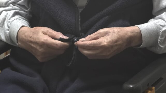 高齢男性が服のジッパーを閉める様子　介護と日常生活のイメージ
