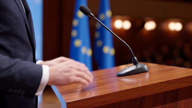 Close-up of hands adjusting a conference microphone before a political speech, blue and gold flags glowing softly behind the podium. Microphone speech preparation concept