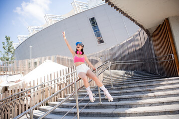 Young woman roller skating on urban stairs in pink crop top and headphones enjoying a sunny summer...