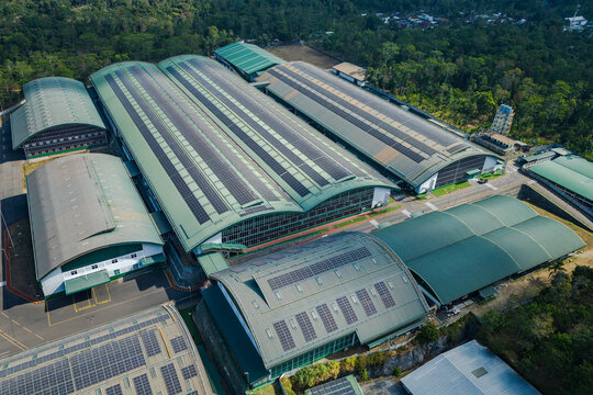 Aerial view of a large industrial factory complex featuring green arched roofs covered with solar panels surrounded by lush greenery in Salatiga, Central Java, Indonesia.