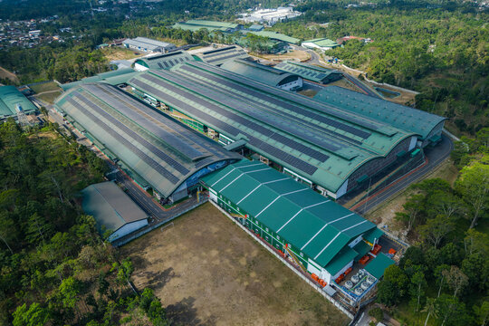 Aerial view of a large industrial factory complex with green roofs and solar panels, surrounded by lush tropical forest in Salatiga, Central Java, Indonesia.