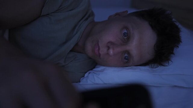 Close up of man endlessly scrolling short form videos on smartphone in bed at night, compulsive social media use and screen addiction
