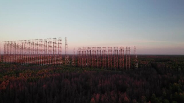 Aerial view of the massive Duga 1 Receiver radar array rising above the dense forest canopy during sunset in Chernobyl, Kyiv Oblast, Ukraine.