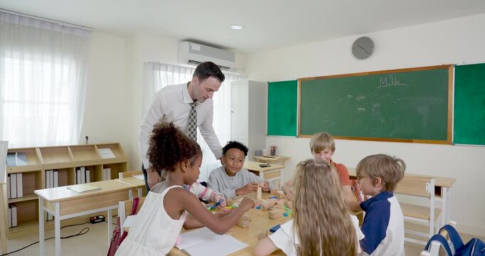 Adult male primary teacher bends over group table guiding multicultural children with colorful blocks, back to school teamwork activity builds math practice, cooperation, confidence, support