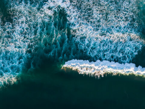 Aerial view of Pacific Ocean waves crashing with white foam patterns on the dark blue water surface in Bandon, Oregon, United States.