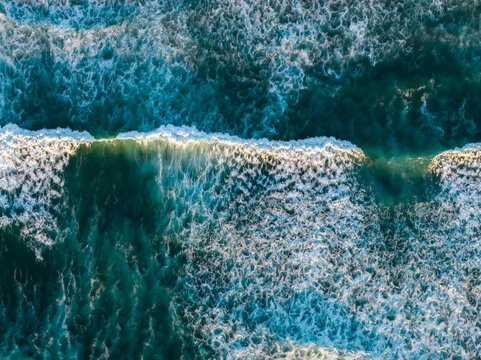 Aerial view of Pacific Ocean waves breaking with white foam and deep blue water in Bandon, Oregon, United States.