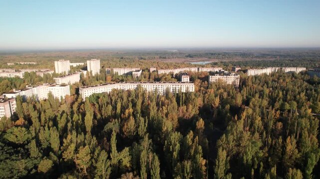 Aerial view of abandoned Soviet-era apartment blocks overgrown with dense autumn forest in the ghost city of Pripyat, Kyiv Oblast, Ukraine.