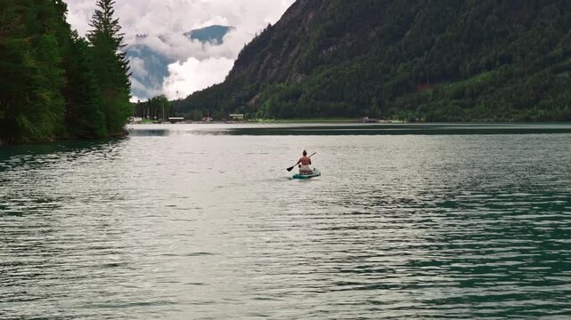 A woman paddleboards on the tranquil waters of Lake Achensee in Tyrol, Austria - drone shot