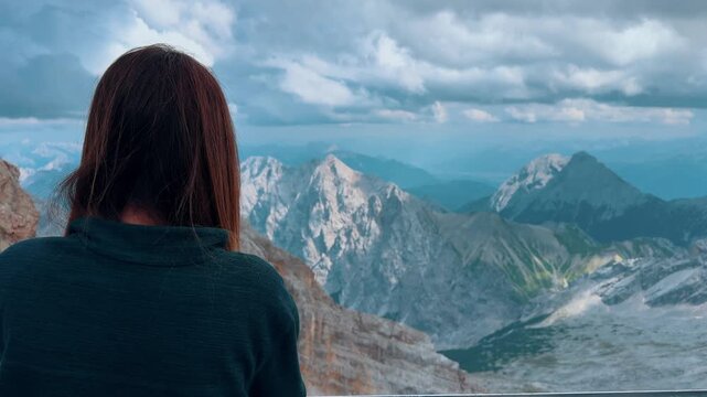 Woman from behind, looking at the stunning panoramic view of the majestic Alps from the Zugspitze summit in Germany