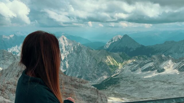 Woman looking at the stunning view from the top of the mountain. Breathtaking scenery of the snowy German Alps on a cloudy day