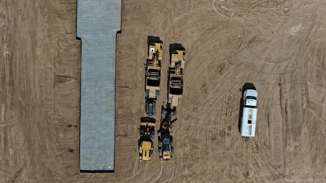 Aerial view of construction machinery including graders and rollers parked on a dirt lot next to a concrete slab in Longmont, Colorado, United States.