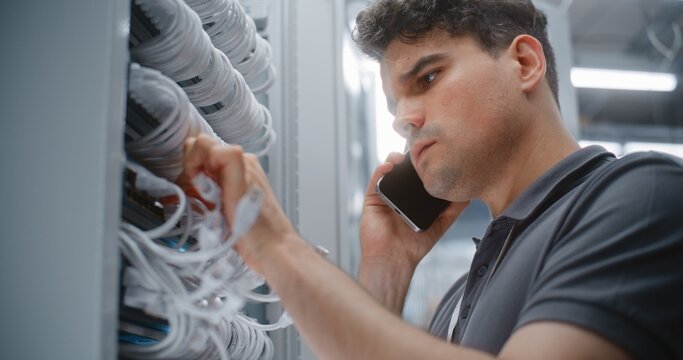 Male IT Technician Reviews Physical Network Connections During Smartphone Call, Confirming Port Identification and Rack Cabling as Part of Coordinated Data Center Infrastructure Audit Process.