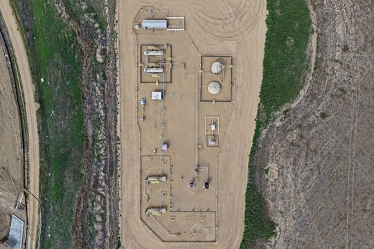 Aerial view of an oil and gas facility with storage tanks, pipelines, and industrial equipment on a dirt pad in the rural landscape of Longmont, Colorado, United States.