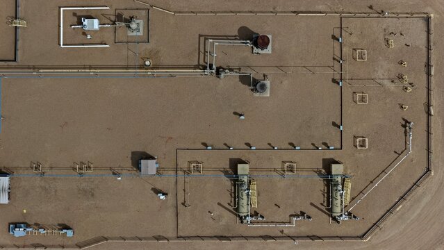 Aerial view of an oil and gas well pad featuring storage tanks, pipelines, and industrial equipment on a dirt surface in Longmont, Colorado, United States.