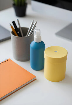 Workplace hygiene and office organization, blue sanitizer spray bottle with yellow storage container and orange notebook on a clean white desk surface