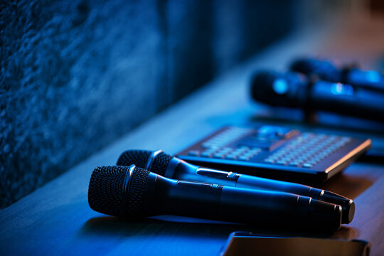 Wireless microphones and audio mixer on wooden table in blue stage light. Professional sound equipment for concert, conference and karaoke. Recording technology concept.