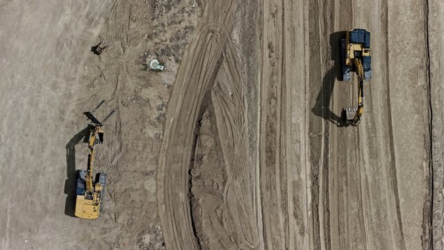 Aerial view of two yellow excavators working on a construction site with tire tracks in the dirt in Longmont, Colorado, United States.
