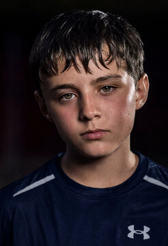 Young athlete in navy sports shirt with wet hair and focused expression, studio portrait with dramatic lighting and dark background