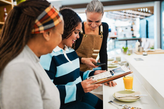 Multiracial women eating inside breakfast bar during morning time - Healthy food and people lifestyle concept - Main focus on center girl - UGC content