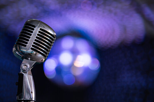 Retro microphone on stage with blue neon lights and smoke. Vintage microphone closeup on concert background with bokeh. Music, singing, karaoke and entertainment concept.