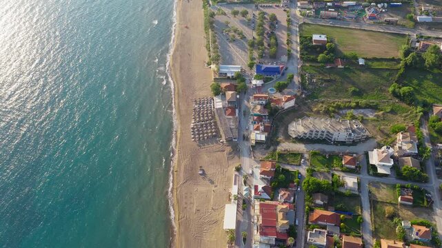 Aerial footage of Kourouta Beach, Ilia, Greece, showcasing golden sand, turquoise waves, sun loungers, vibrant village life, and a tranquil Mediterranean summer atmosphere.
