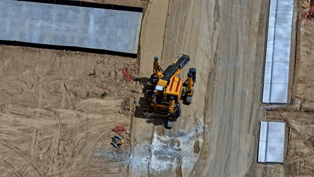 Aerial view of a yellow construction machine working on a dirt site with concrete curbs and pavement sections in Longmont, Colorado, United States.