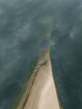An abstract aerial perspective showcases a sharp sandbar dividing two distinct bodies of water, one deep blue and the other a murky green
