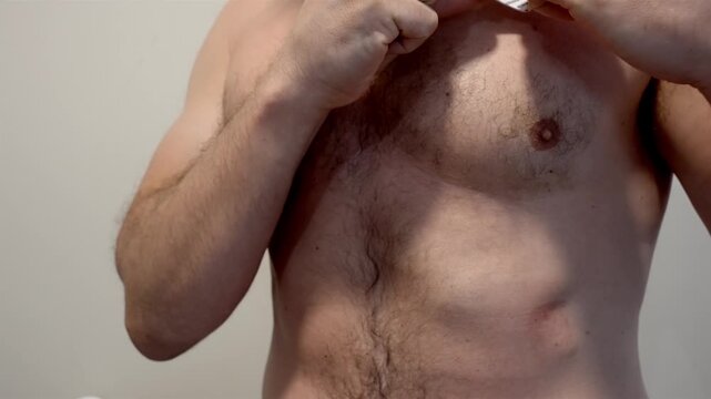 Heart monitor pads are applied by hand to a bare male chest indoors.
