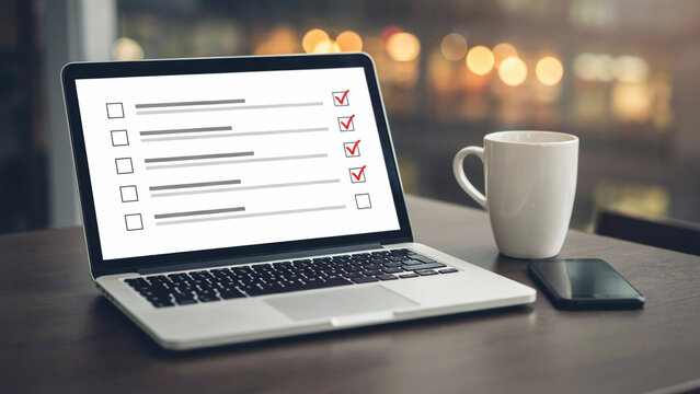 Laptop with checklist on screen during evening with coffee cup and phone on desk