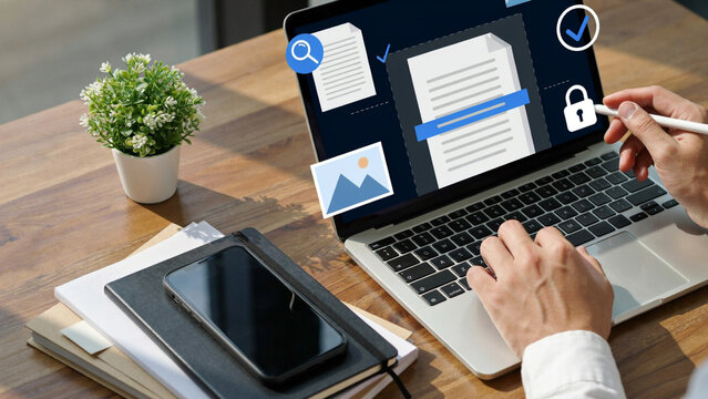 Person's hands typing on laptop showing digital document management interface with icons on desk during daytime