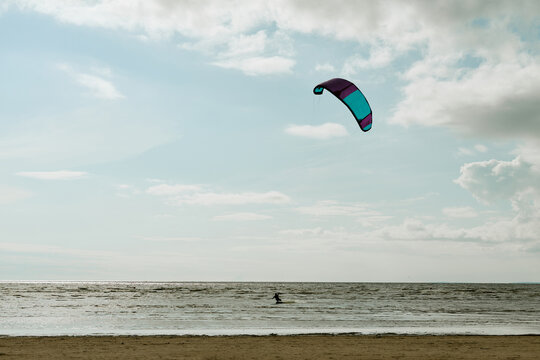 Distant kitesurfing across ocean waves under cloudy sky, wide shot. Concept represents active recreation, outdoor adventure, suitable for extreme sports tourism marketing