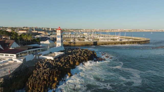 Aerial view of Santa Marta Lighthouse and Cascais marina with moored yacht boats with Cascais cityscape, Portugal on sunset. Orbit parallax shot
