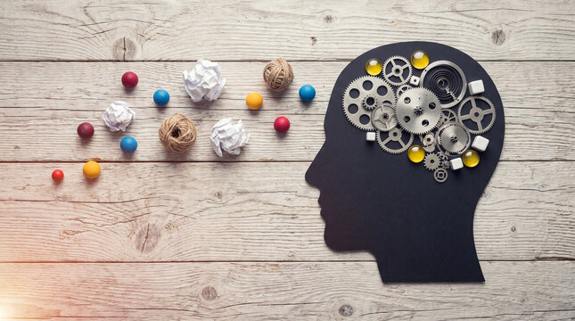 Black head silhouette with shiny metallic gears and colorful paper balls on rustic wood.