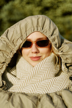 Portrait of young adult Caucasian woman wearing sunglasses and winter hood outdoors. Ideal visual for cold weather fashion campaigns and lifestyle product branding, vertical