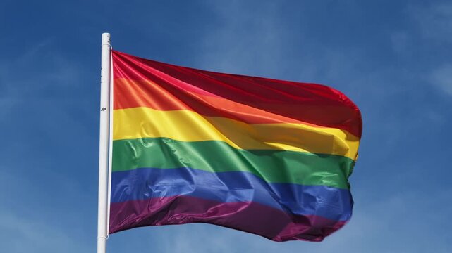 Rainbow pride colors wave on a traditional pride flag in the Lisbon, Portugal sky for LGBT equality, with windblown fabric in bright afternoon light
