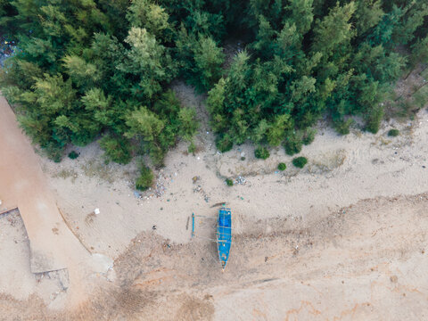 Aerial view of a blue fishing boat on the sandy shore of Guhagar Beach, bordered by lush green trees Guhagar, Maharashtra, India.