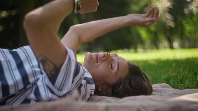 Caucasian young woman lying on blanket, practicing mindfulness relaxation during outdoor therapy session in park. Ideal for mental wellness campaigns, stress relief ads, and healthcare services