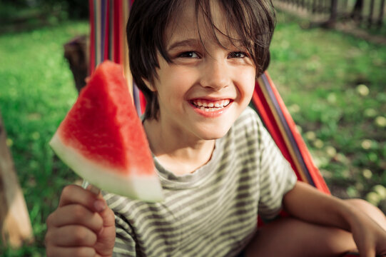 Happy boy holds a fresh watermelon slice outdoors in summer