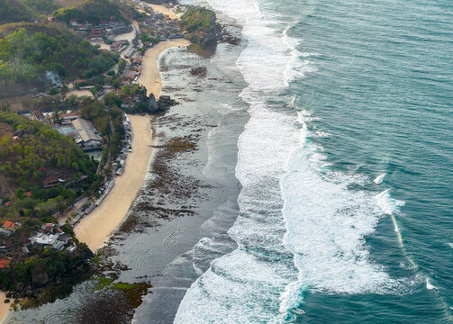 Aerial view of the coastline in Gunungkidul Regency, featuring sandy beaches, rocky outcrops, and waves crashing against the shore in Special Region of Yogyakarta, Indonesia.