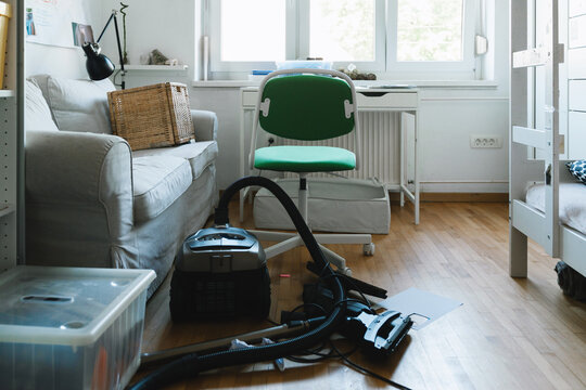 A vacuum cleaner and packed boxes sit on the wooden floor of a messy living room during a move. Authentic home relocation and spring cleaning concept.