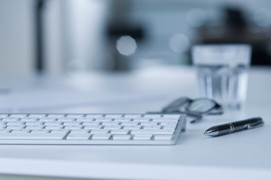 Keyboard on desk, water glass, ballpen and spectacles
