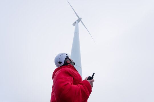 Technician inspecting wind turbine outdoors wearing helmet and red jacket