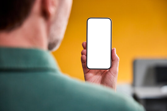 Businessman holds smartphone with blank screen in office