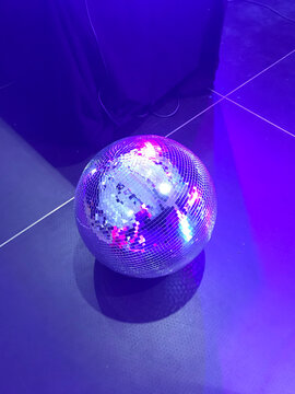 Shiny disco ball on the floor illuminated by purple neon light