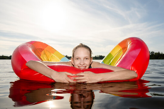 A smiling girl floats on a colorful swimming aid in a sunny lake